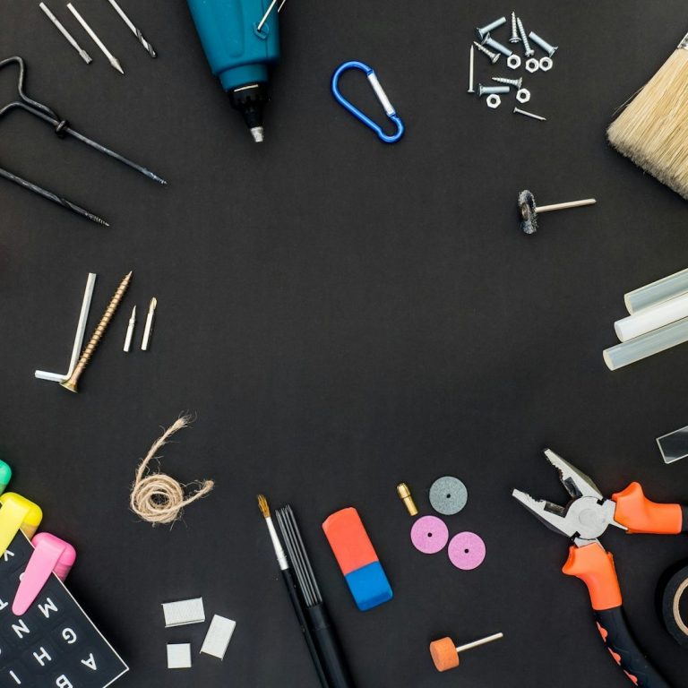 A collection of various tools, screws, and craft supplies arranged on a black surface.